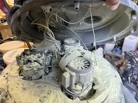 Technician inspecting damaged motor and electrical components inside concrete vacuum equipment during repair diagnostics.